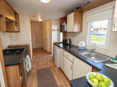 A narrow kitchen with wooden cabinets countertop appliances and a bowl of green apples on the counter at 15 Rosewood Great Thorness near Northwood Isle Of Wight