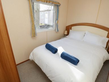 A bedroom with a double bed white bedding two blue towels on the bed a bedside table with a lamp and a window with curtains at 15 Rosewood in Great Thorness near Northwood Isle Of Wight