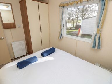 A bedroom with a double bed two rolled towels a wardrobe and a window with curtains at 15 Rosewood Great Thorness near Northwood Isle Of Wight