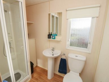 A bathroom with a shower, sink with mirror, toilet, and window at 15 Rosewood Great Thorness near Northwood Isle Of Wight