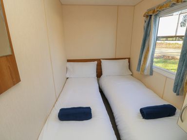 A bedroom with two single beds each with a white pillow and blue towel by a window at 15 Rosewood Great Thorness near Northwood Isle Of Wight