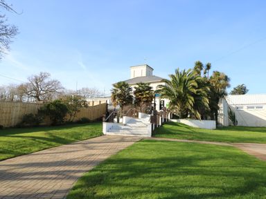 A building with steps leading up to it surrounded by palm trees and green grass at 15 Rosewood in Great Thorness near Northwood Isle Of Wight