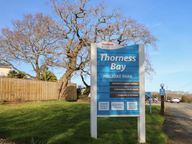 A sign for Thorness Bay Holiday Park by Parkdean Resorts next to a grassy area and trees at 15 Rosewood Great Thorness near Northwood Isle Of Wight
