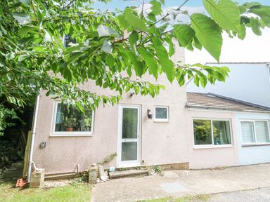 A house exterior with a door and several windows partially covered by tree branches at Mermaid Cottage in Wakeham Portland