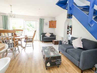 A living room with grey sofas and a wooden dining table near a sliding glass door at Mermaid Cottage in Wakeham Portland