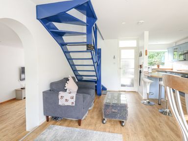 A living room and kitchen area with a blue metal staircase a gray sofa and a wooden table at Mermaid Cottage in Wakeham Portland