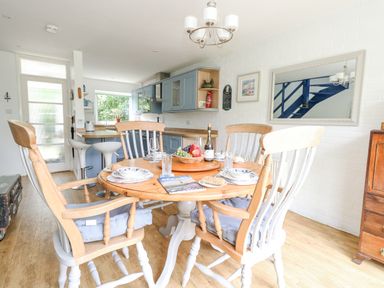 A kitchen dining area with a wooden round table set for four and blue cabinets at Mermaid Cottage in Wakeham Portland
