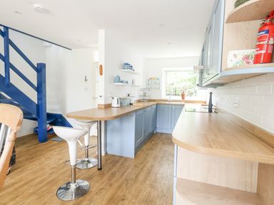 A kitchen with blue cabinets wooden countertops and white bar stools at Mermaid Cottage in Wakeham Portland