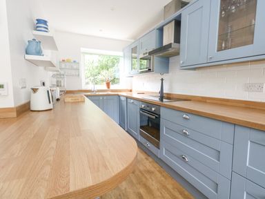 A kitchen with blue cabinets wooden countertops white walls and shelves at Mermaid Cottage in Wakeham Portland