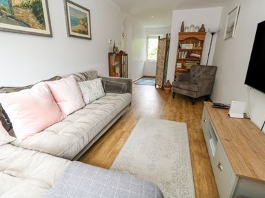 A living room with a gray sofa with pink cushions a brown armchair a wooden bookshelf and a television on a wooden cabinet at Mermaid Cottage in Wakeham Portland