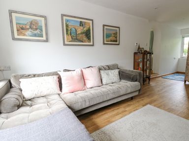 A living room with a gray sofa and framed landscape paintings on the wall at Mermaid Cottage in Wakeham Portland