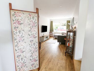 A living room with a floral divider a wall-mounted tv a sofa and a glass display cabinet at Mermaid Cottage in Wakeham Portland
