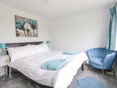 A bedroom with a double bed with white bedding and blue towels on it two bedside tables with lamps a blue armchair blue curtains and a blue rug Mermaid Cottage Wakeham Portland