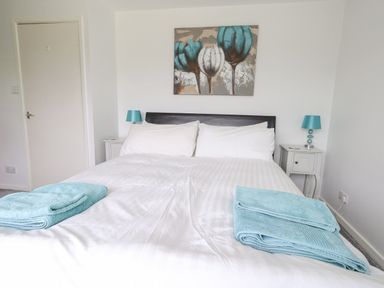 A bedroom with a double bed white bedding and teal towels bedside tables with lamps and a painting above the bed at Mermaid Cottage in Wakeham Portland