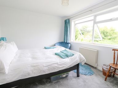 A bedroom with a bed white bedding teal towels a teal chair a wooden chair and a window with curtains at Mermaid Cottage in Wakeham Portland
