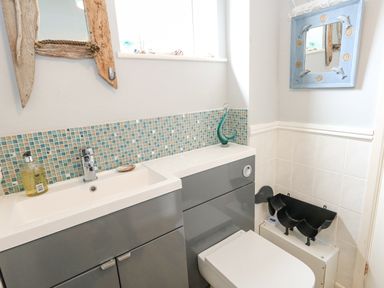 A bathroom with a grey vanity unit sink and toilet with mosaic tile backsplash and two mirrors at Mermaid Cottage in Wakeham Portland