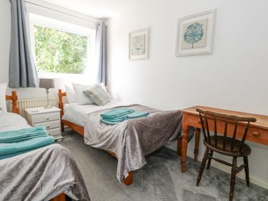 A bedroom with two single beds a wooden desk a wooden chair and framed pictures on the wall at Mermaid Cottage in Wakeham Portland
