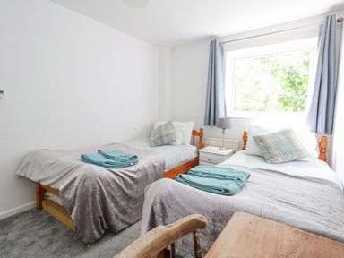 A bedroom with two single beds with blankets and pillows a nightstand with a lamp and a window with curtains at Mermaid Cottage in Wakeham Portland