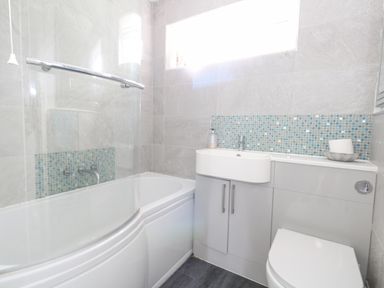A bathroom with a bathtub shower combination a sink with cabinets and a toilet at Mermaid Cottage in Wakeham Portland