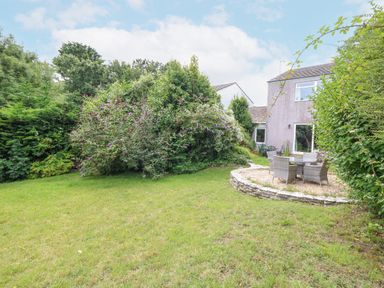 A garden with green grass shrubs and a patio area with outdoor furniture at Mermaid Cottage in Wakeham Portland