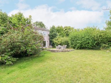 A garden with grass bushes and a stone patio with chairs at Mermaid Cottage in Wakeham Portland