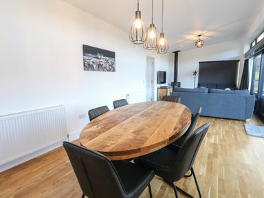 A dining area with a wooden table and black chairs next to a living room with blue sofas and a wood stove at Osprey View Lodge & Hot Tub Aberfeldy