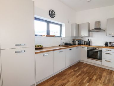 A kitchen with white cabinets wooden countertops a clock above a window and stainless steel appliances at Osprey View Lodge & Hot Tub in Aberfeldy