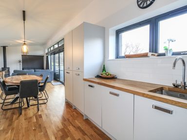 A kitchen with wood countertops and white cabinets next to a dining table with black chairs at Osprey View Lodge & Hot Tub Aberfeldy