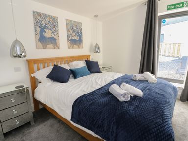 A bedroom with a wooden bed frame white bedding blue cushions and a navy blanket with rolled towels a mirrored nightstand and two deer paintings at Osprey View Lodge & Hot Tub Aberfeldy