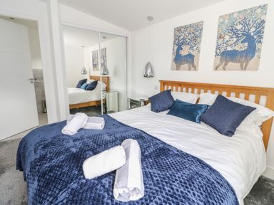 A bedroom with a bed covered in blue bedding and rolled towels with mirrored closet doors and animal artwork on the wall at Osprey View Lodge & Hot Tub in Aberfeldy
