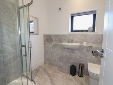 A bathroom with a corner shower, wall-mounted sink, toilet, and a window at Osprey View Lodge & Hot Tub Aberfeldy