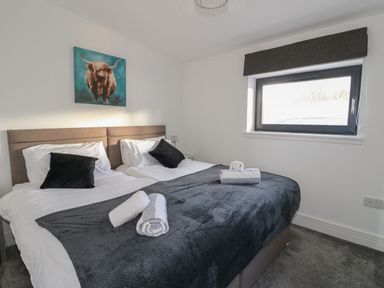 A bedroom with a double bed with black pillows towels on the bed and a painting above the headboard at Osprey View Lodge & Hot Tub in Aberfeldy