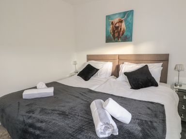 A bedroom with a double bed with white and black bedding and a painting of a bull above the bed at Osprey View Lodge & Hot Tub in Aberfeldy
