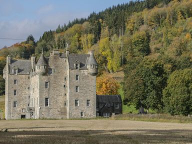 A stone castle with turrets and multiple windows near a forested hillside at Osprey View Lodge & Hot Tub in Aberfeldy