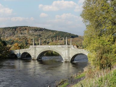 A stone arch bridge over a river with hills and trees in the background at Osprey View Lodge & Hot Tub in Aberfeldy