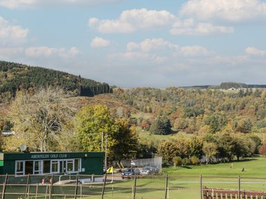 A golf course with a building labeled Aberfeldy Golf Club and hills with trees in the background at Osprey View Lodge & Hot Tub in Aberfeldy