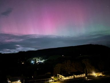 A night sky with northern lights above a dark hillside and buildings with lights at Osprey View Lodge & Hot Tub in Aberfeldy