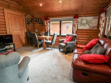 A living room with a dining table chairs an armchair and a sofa with red cushions at 10 Waters Edge Morpeth near Felton