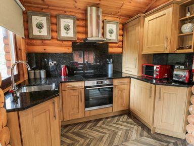 A kitchen with wooden cabinets black countertops a stainless steel oven red kitchen appliances and framed art on wood walls at 10 Waters Edge Morpeth near Felton