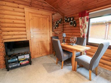 A small dining area with a wooden table and four grey chairs next to a window in a log cabin at 10 Water's Edge Morpeth near Felton