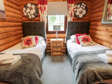 A bedroom with two single beds separated by a wooden nightstand with a lamp at 10 Water's Edge in Morpeth near Felton