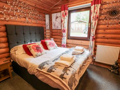 A bedroom with a bed with pillows and towels by a window with floral curtains at 10 Waters Edge Morpeth near Felton