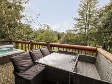 An outdoor deck with a glass top table and wicker seating surrounded by trees at 10 Waters Edge Morpeth near Felton