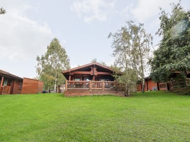 A wooden log cabin with a porch surrounded by green grass and trees at 10 Waters Edge Morpeth near Felton