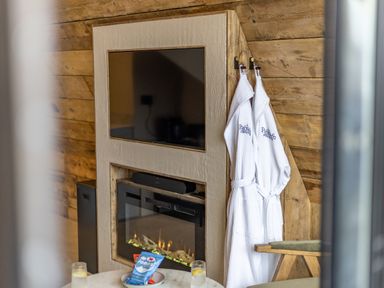 A wall-mounted television above a fireplace with two white robes hanging on hooks by a wooden wall at The Tri-Pod Pantcefn near Llanarth