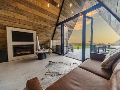 An interior living space with a fireplace a round table and brown sofa next to glass doors opening to an outdoor deck at The Tri-Pod in Pantcefn near Llanarth