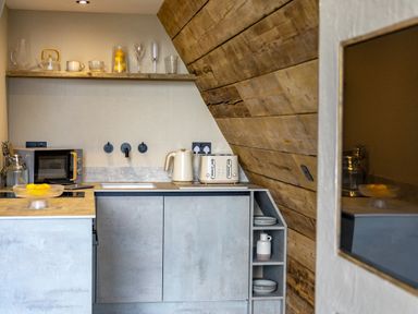 A kitchen with a wooden slanted ceiling microwave kettle toaster and glassware on a shelf at The Tri-Pod in Pantcefn near Llanarth