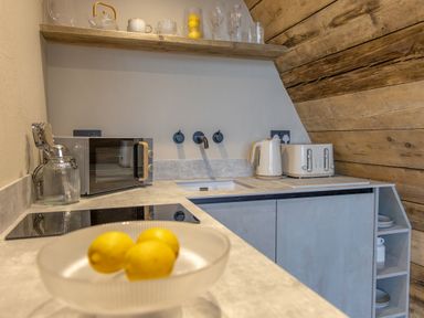 A kitchen countertop with lemons in a bowl a microwave kettle toaster and open shelves with plates at The Tri-Pod in Pantcefn near Llanarth