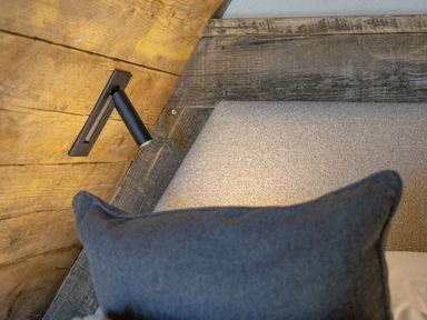 A wall-mounted reading light above a bed with a grey upholstered headboard and a blue pillow at The Tri-Pod in Pantcefn near Llanarth