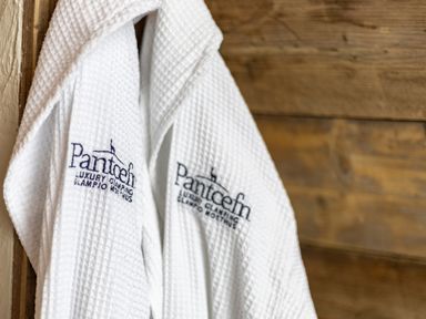 Two white bathrobes hanging on wooden hooks with Pantcefn Luxury Glamping branding